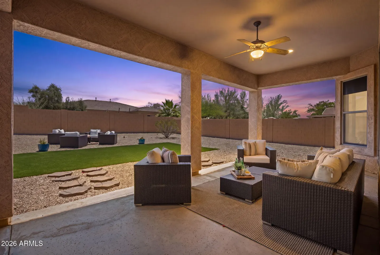 Covered patio with wicker furniture, ceiling fan, and view of backyard with seating area at dusk.