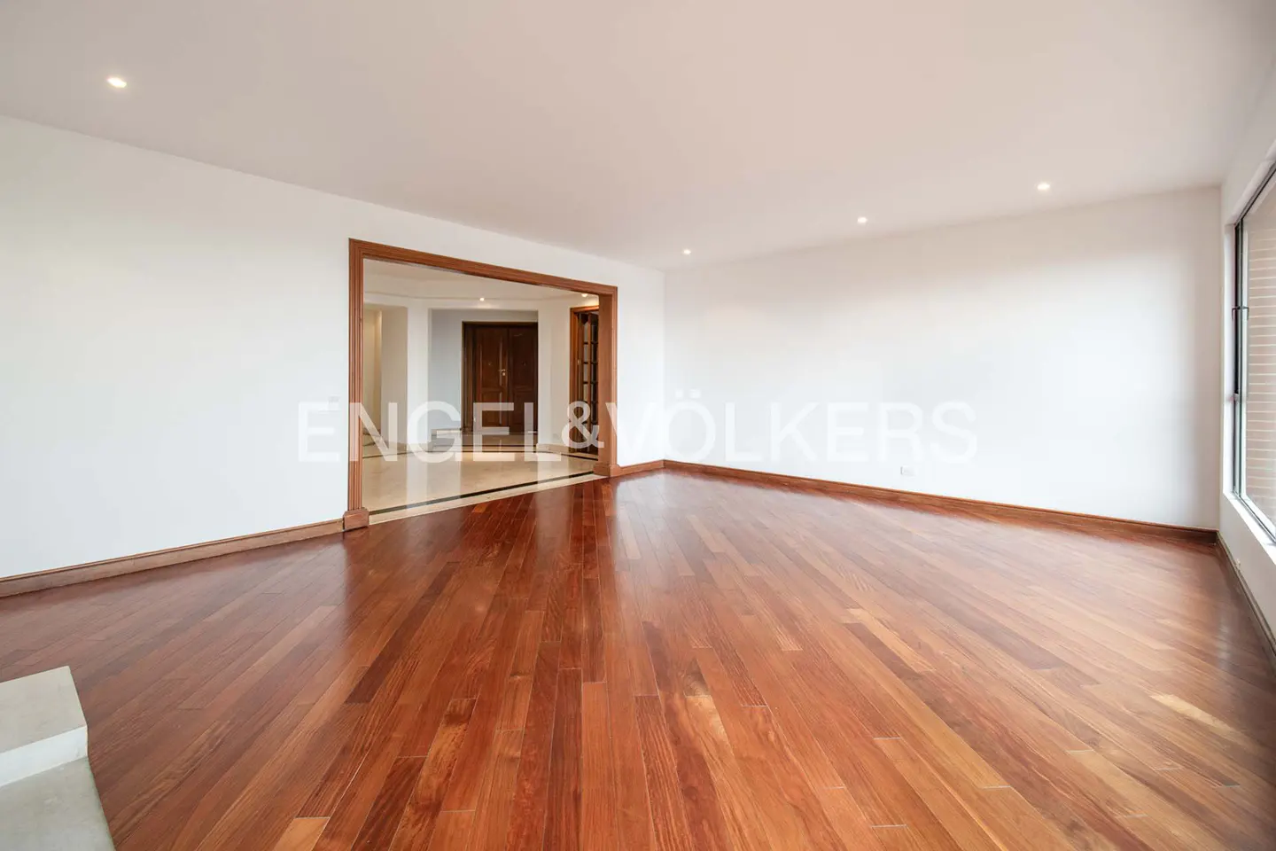 An empty room with hardwood floors, white walls, and a doorway to another room.
