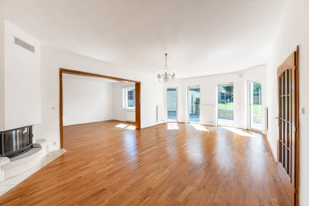 Bright, empty living room with hardwood floors, white walls, fireplace, chandelier, and doors leading to the outside.