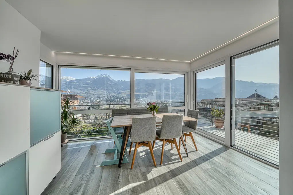 Bright dining room with wood floors, table, and gray chairs. Large windows offer mountain views. A white cabinet is on the left.