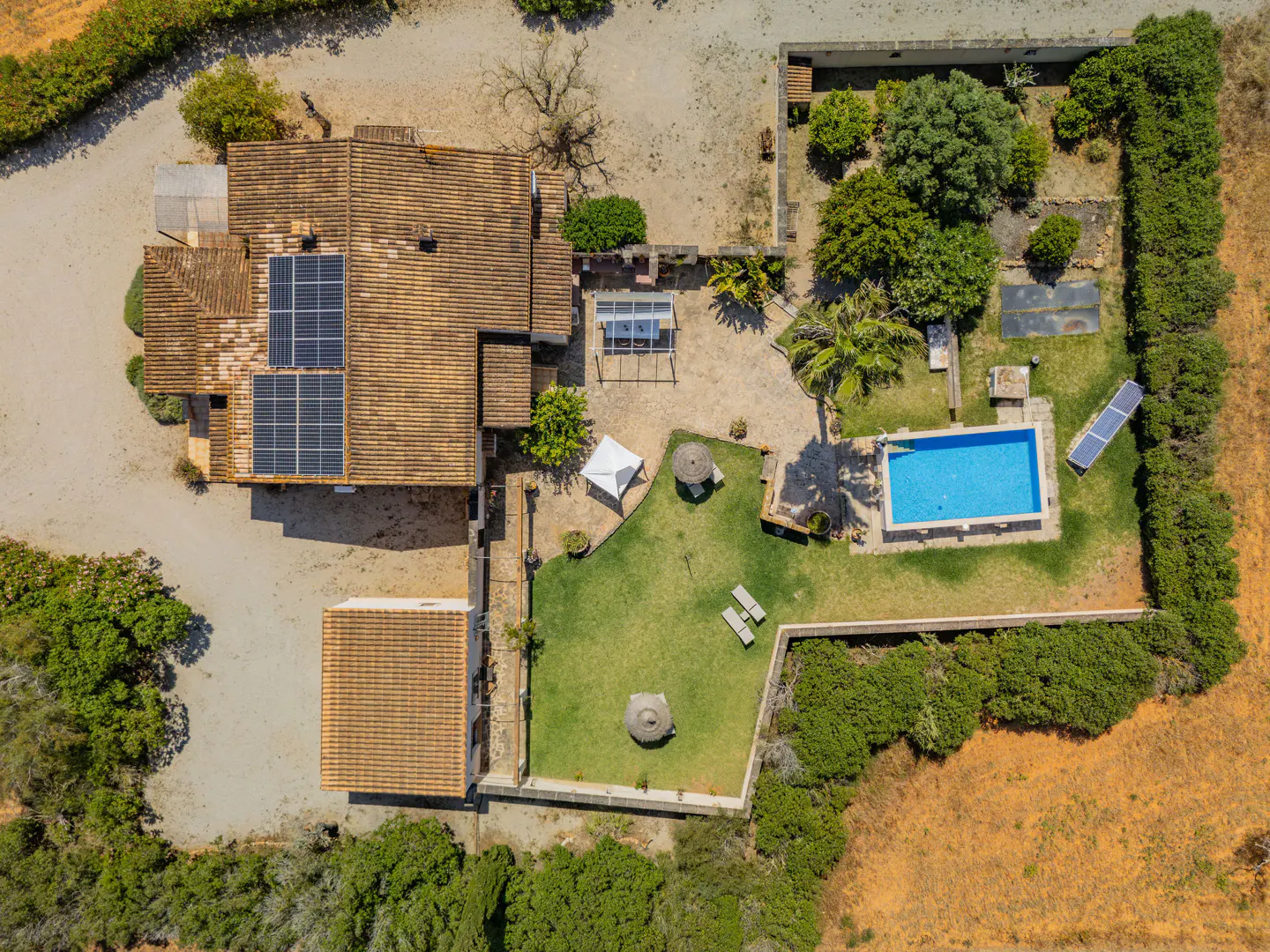 Aerial view of a property with a terracotta-tiled roof, solar panels, pool, and green lawn.