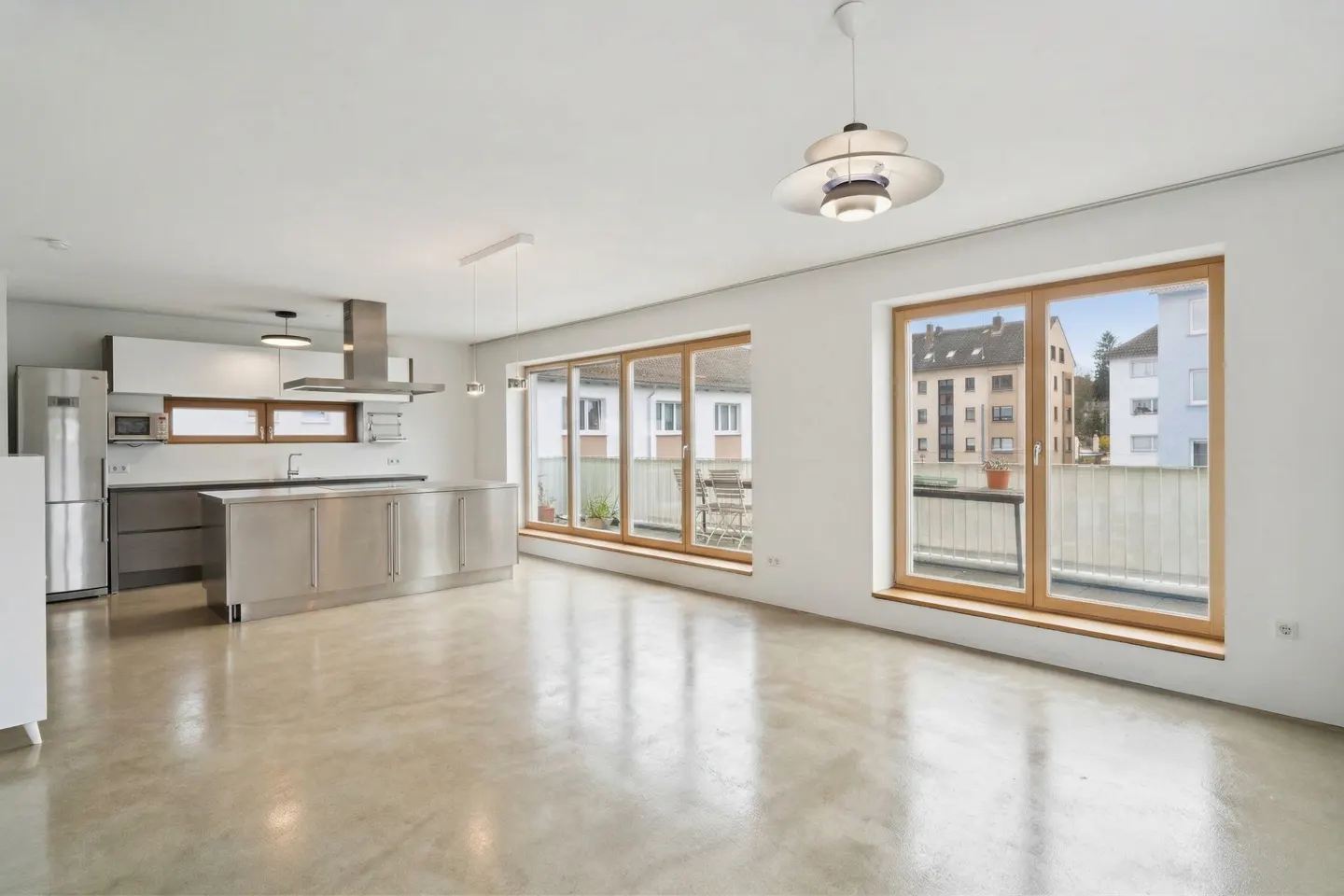 Bright, modern apartment with stainless steel kitchen island, white cabinets, and large windows overlooking a balcony and city buildings.