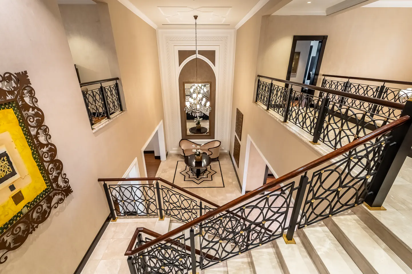 View from above of a beige foyer with stairs, black railings, and a seating area with a mirror and chandelier.
