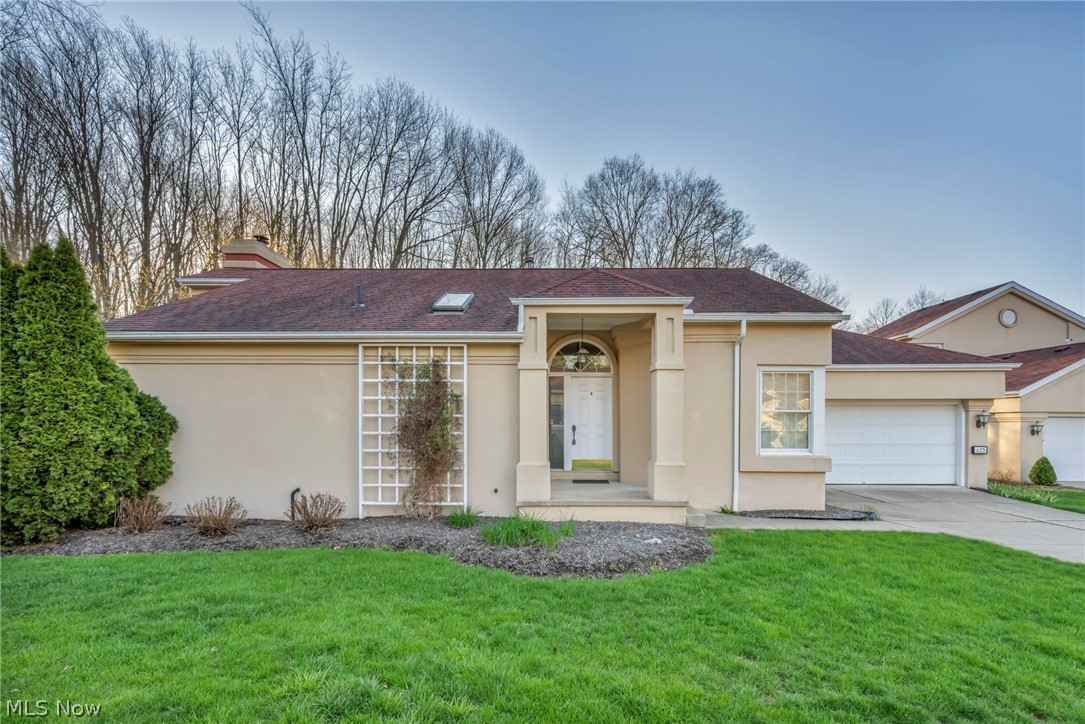Beige single-story home with a red roof, white door, and a green lawn. Trees are visible in the background.