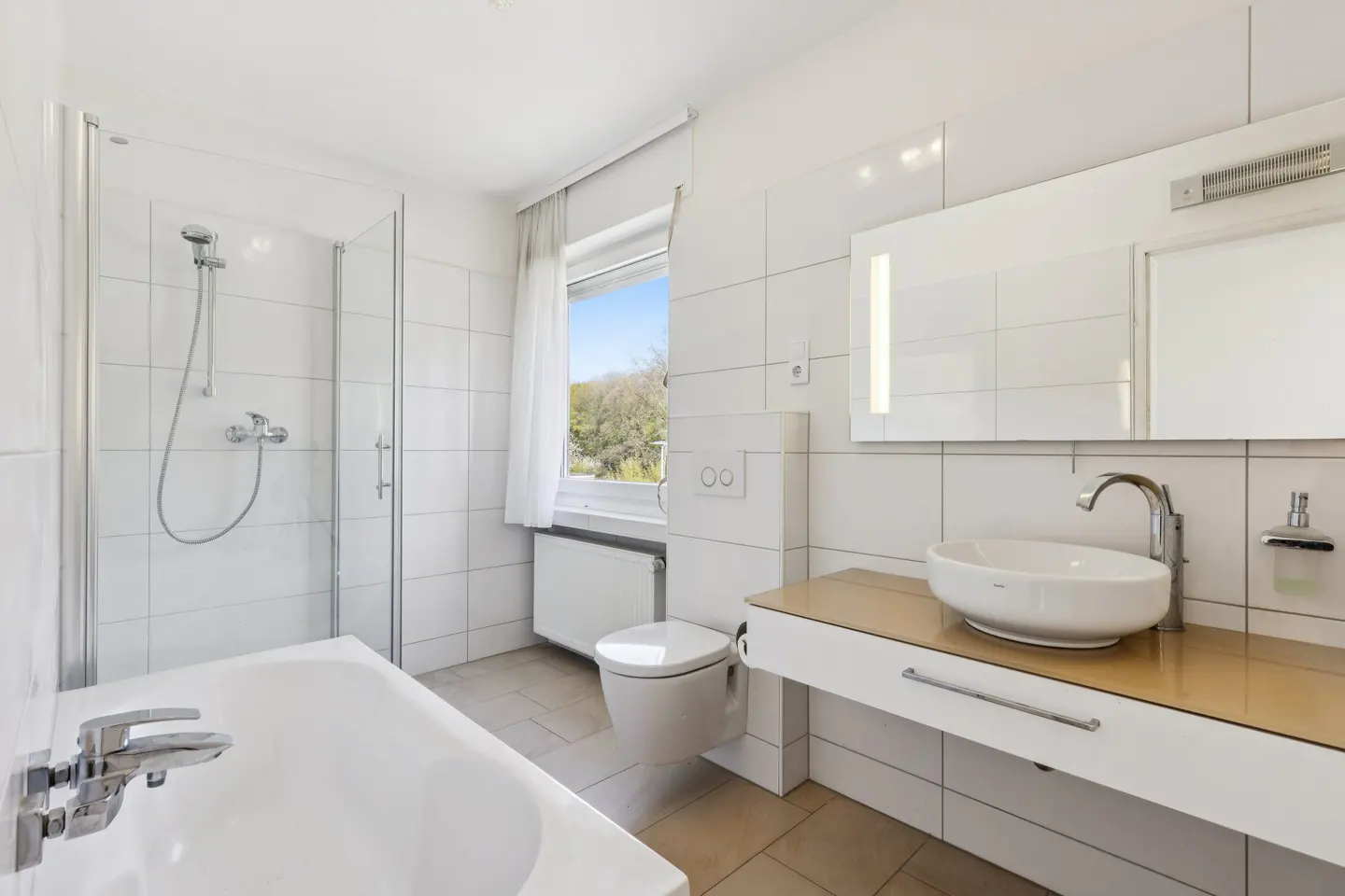 Bright bathroom with white tile walls, a tub/shower with glass door, toilet, and sink with a wood-look countertop.
