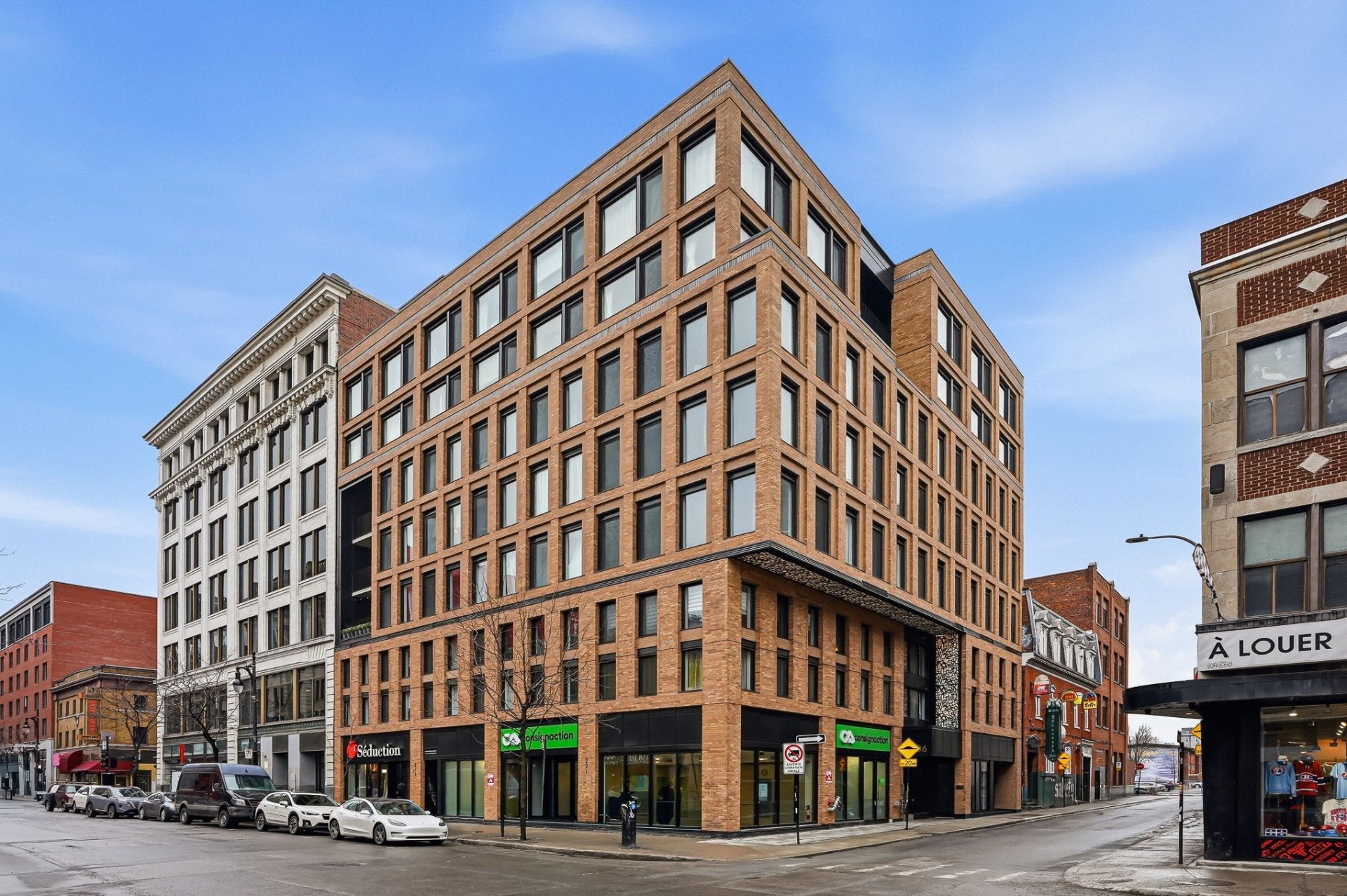 Modern brick commercial building on a city street corner with large windows and ground-floor retail spaces under a blue sky. [AI-generated text]