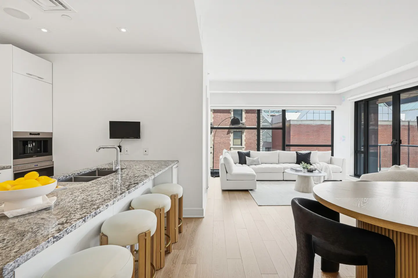 Open-concept living space with a kitchen island, white cabinets, granite countertops, and a living room with a white sectional sofa.