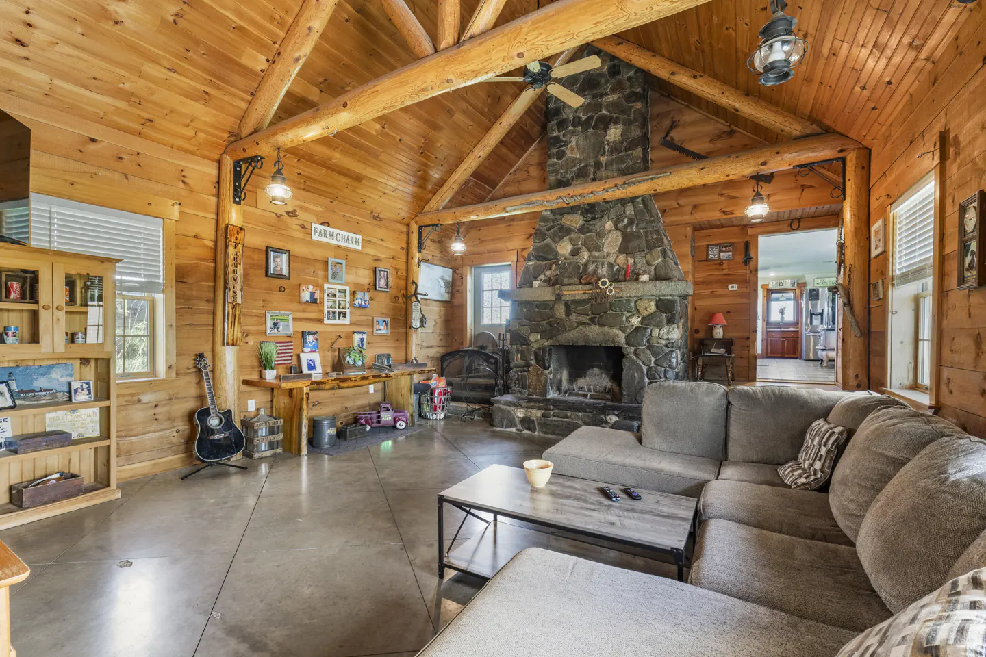 Rustic living room with wood walls, stone fireplace, and gray sectional sofa.