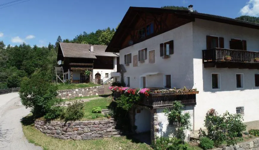 Two-story white house with brown trim and balconies, surrounded by stone walls and greenery.