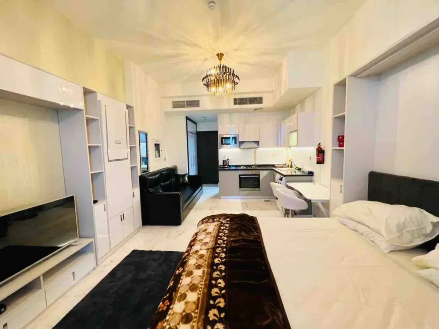 A modern studio apartment with a bed, black sofa, white cabinets, and a small kitchen.