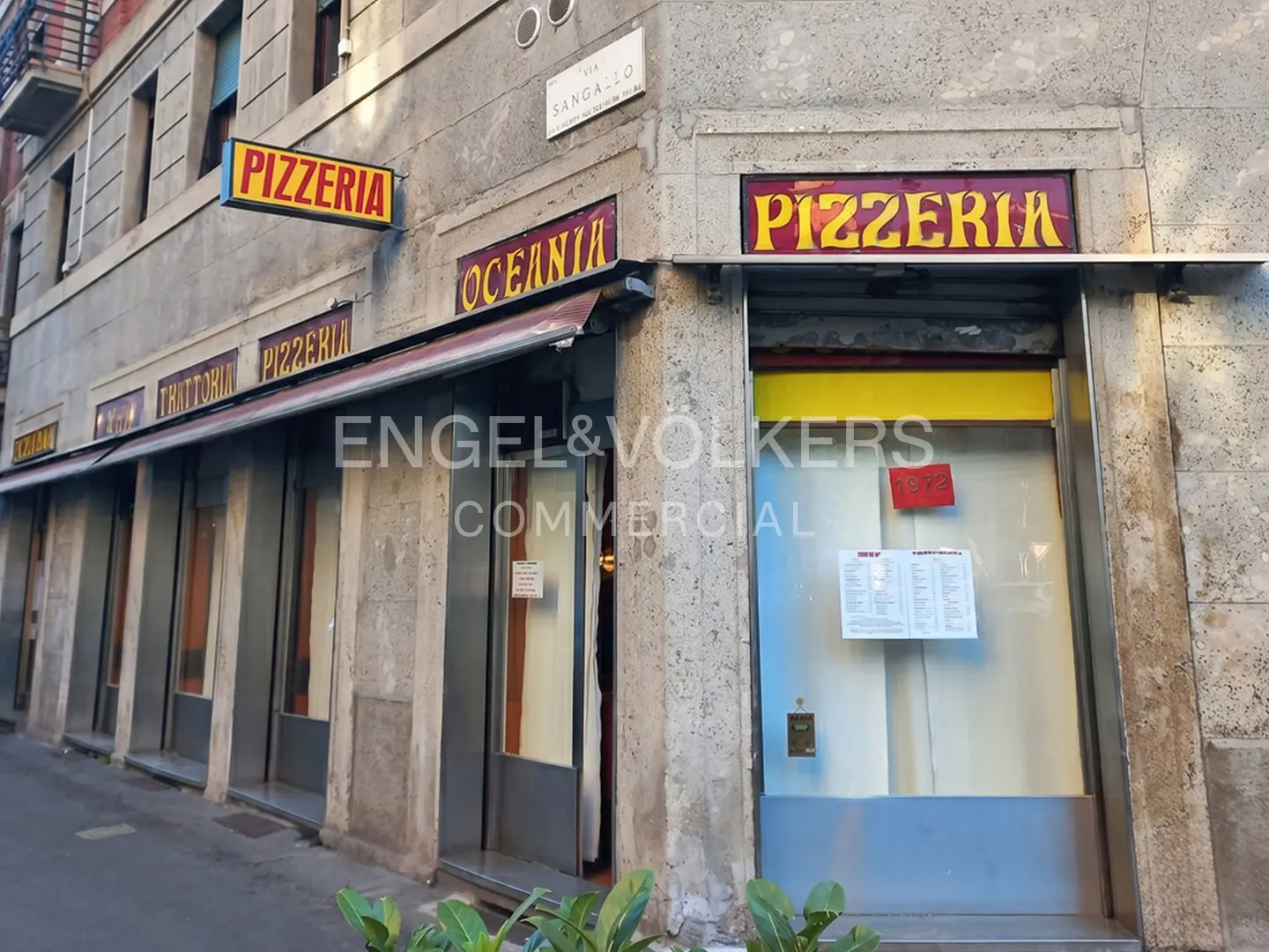 Exterior view of a "Pizzeria Oceania" restaurant with yellow and red signage on a stone building.