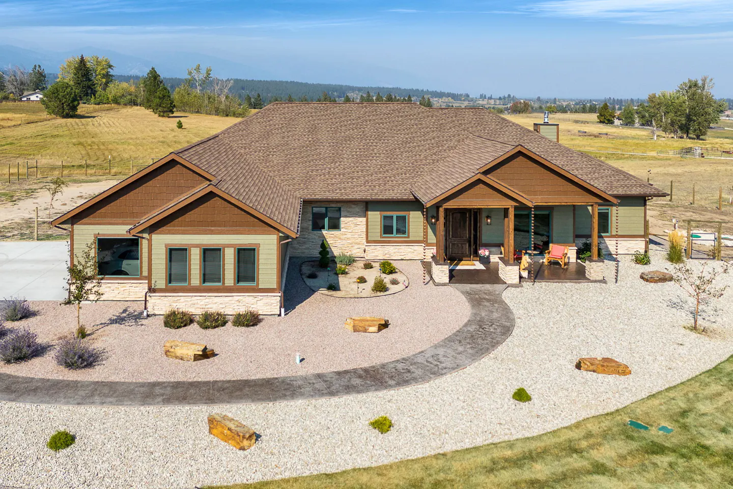 Aerial view of a one-story home with a brown roof, green siding, and a stone walkway leading to the front porch.