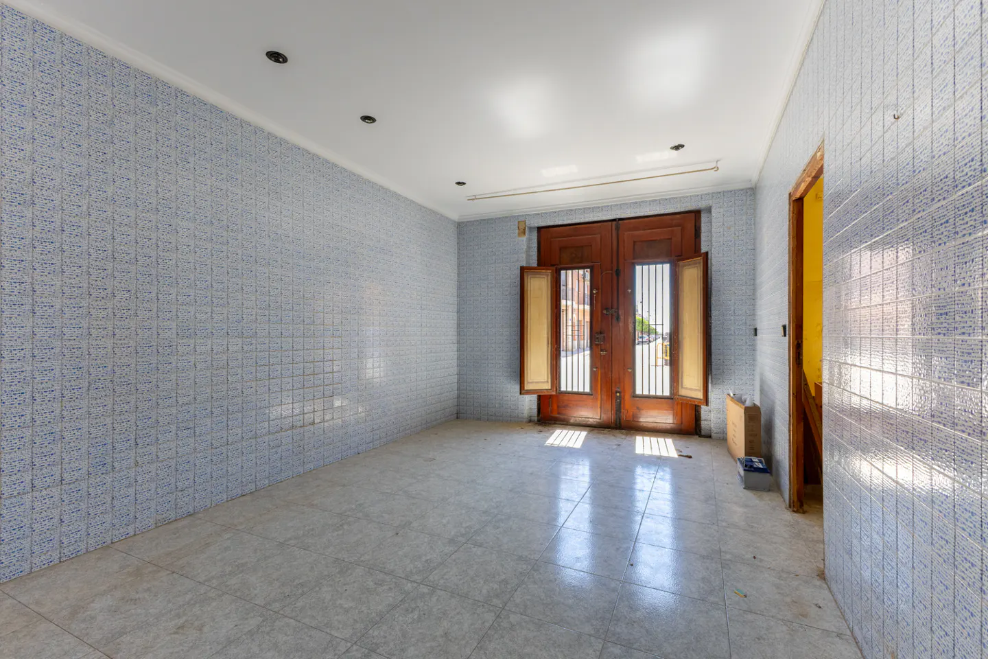 Empty room with blue tiled walls and floor. Double wooden doors are open, letting in light.