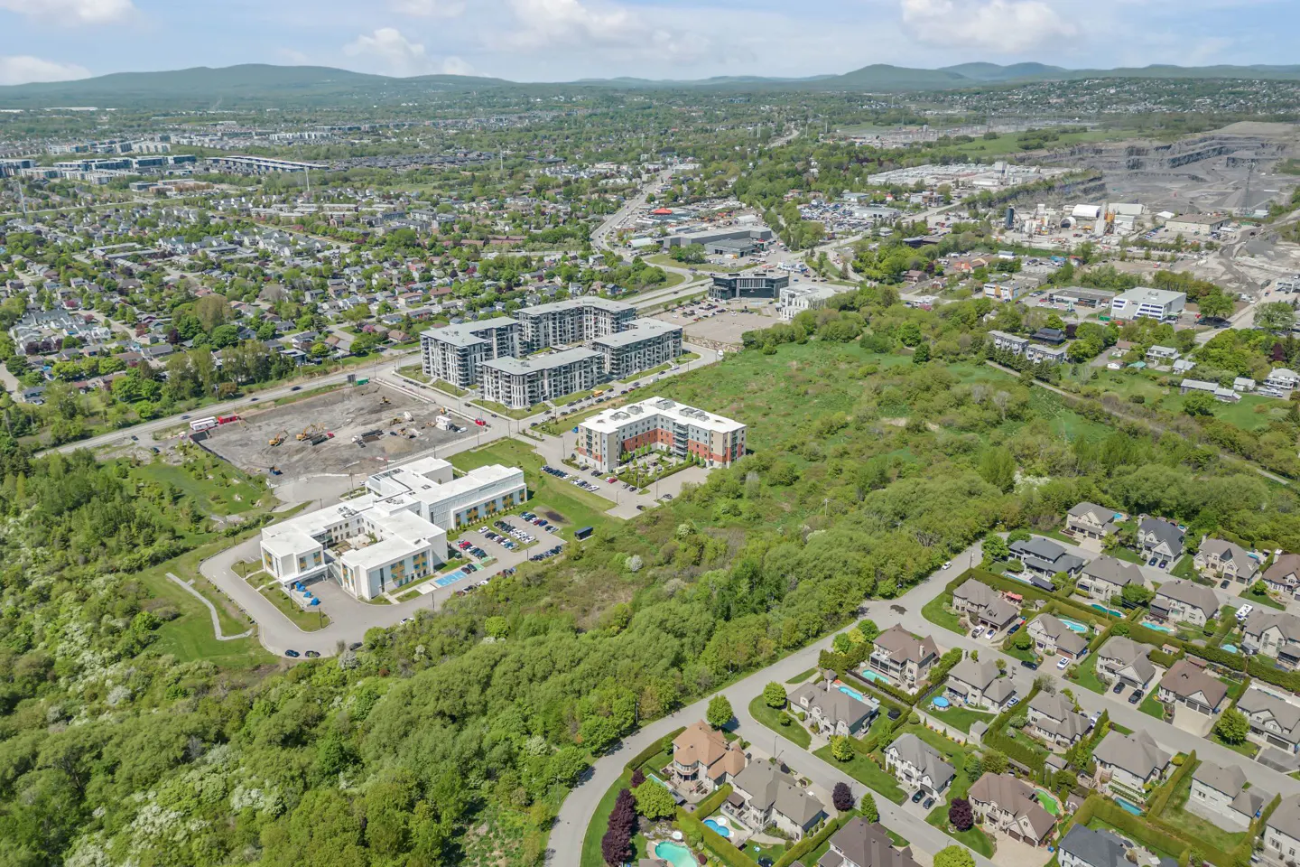 Aerial view of a suburban neighborhood with modern apartment complexes, residential houses, and green spaces under a blue sky.