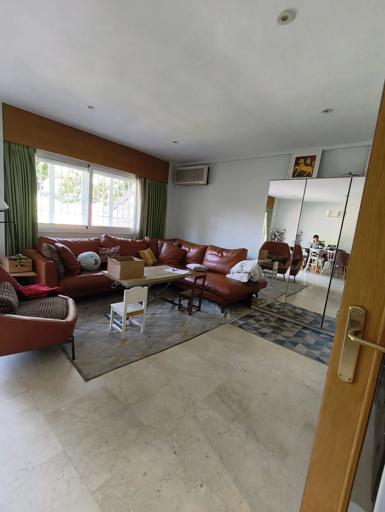 Living room with a large brown leather sectional sofa, a rug, and a white child's chair. A mirror reflects the room.