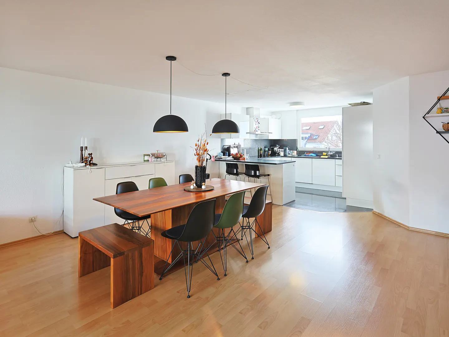 Open-concept living space with wood floors, a dining table with black chairs, and a white kitchen in the background.
