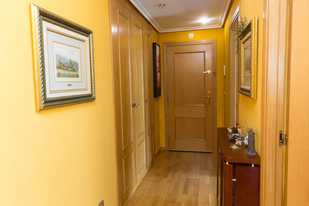 Hallway with yellow walls, wooden floors, and a brown front door. A framed painting hangs on the wall.
