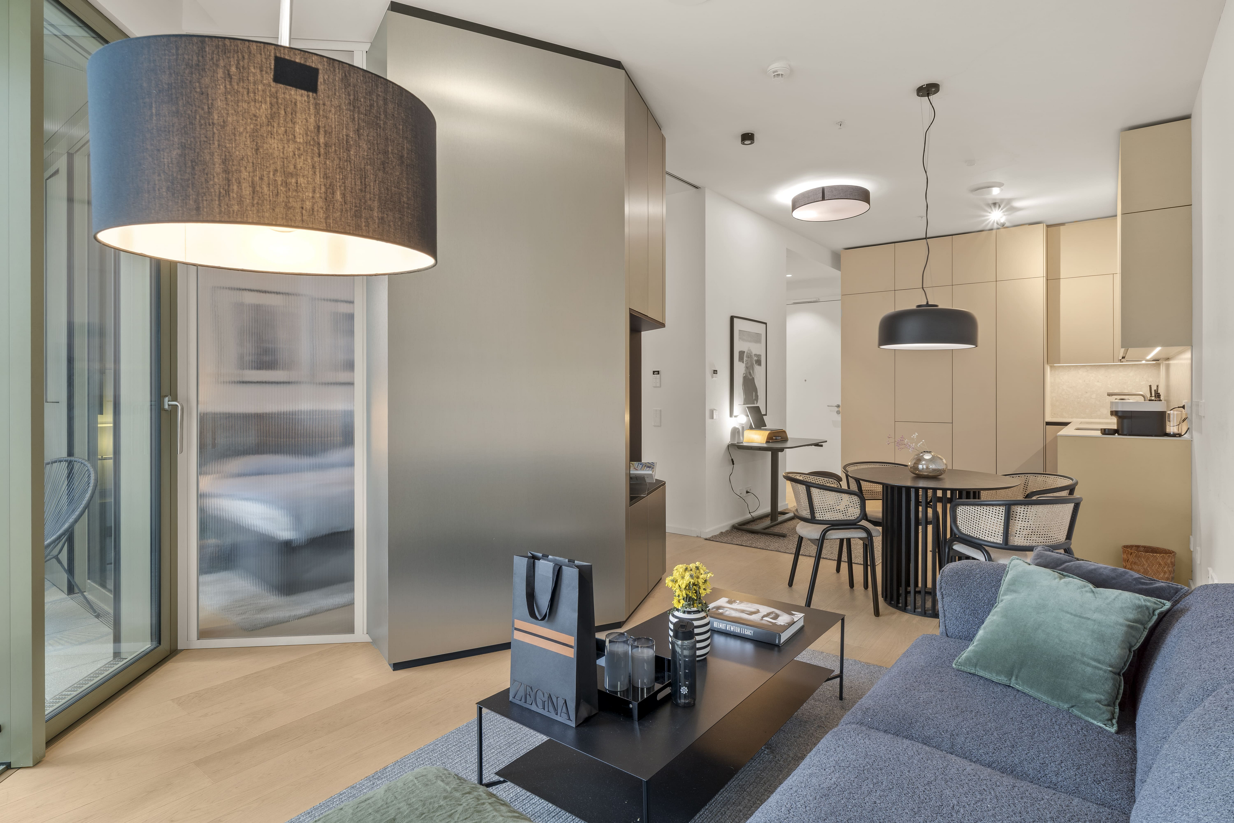 Modern apartment living area with a grey sofa, black coffee table, dining set, and a large metallic room divider.