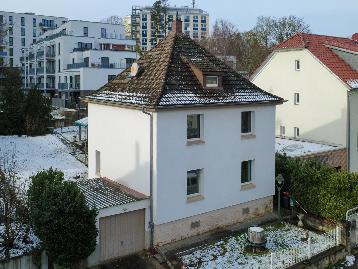 Two-story white house with a brown tile roof and a detached garage. Snow is visible in the yard.
