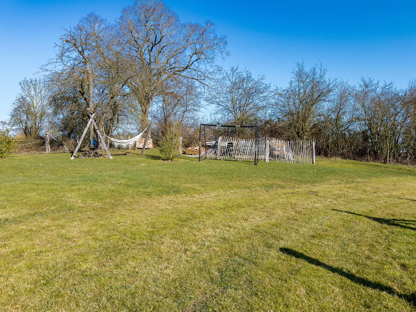 Lawn with hammock, swing set, and trees under a blue sky. A wooden fence is in the background.