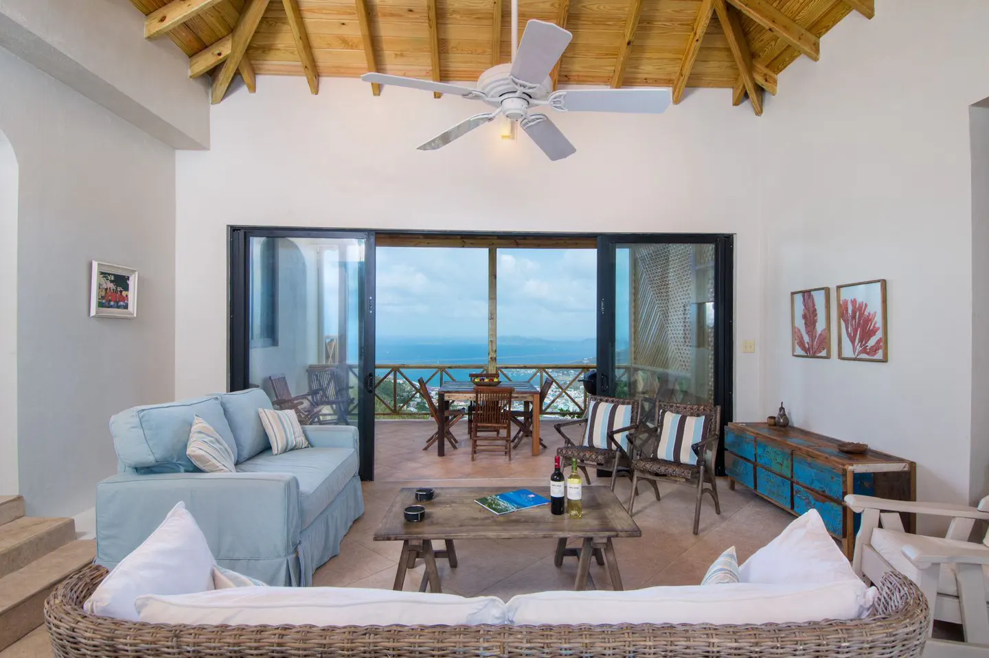 Living room with a light blue sofa, wicker furniture, and a view of the ocean through sliding glass doors.