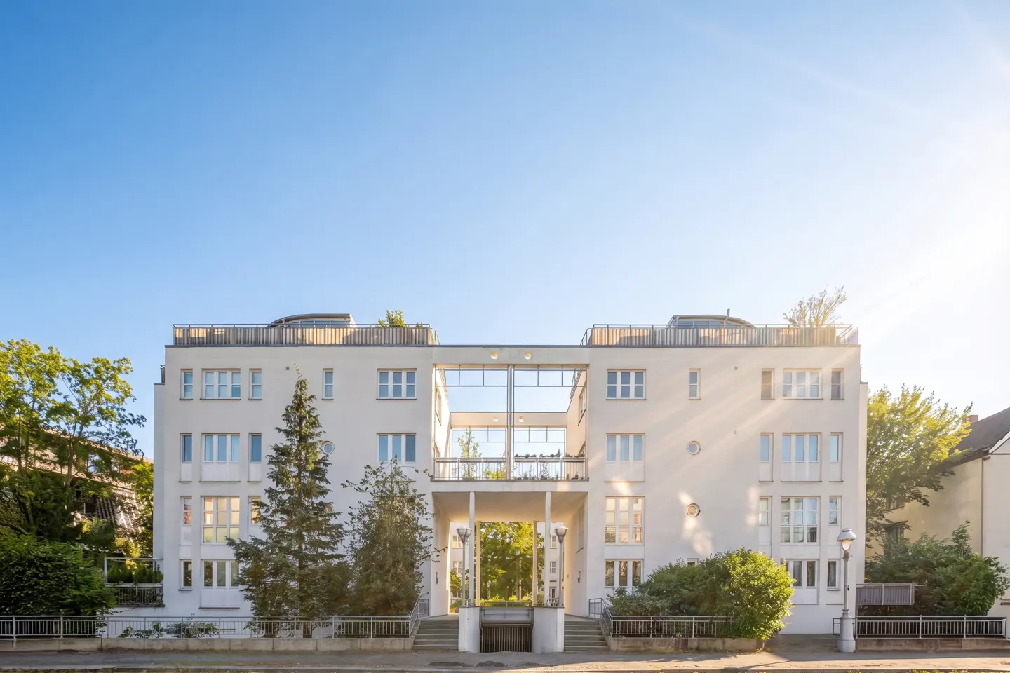 Exterior of a white, multi-story apartment building with a central archway and a bright blue sky.
