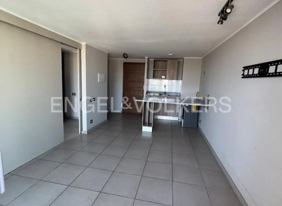 A bright, empty apartment with gray walls, tile floors, and a small kitchen area. A sliding door is on the left.