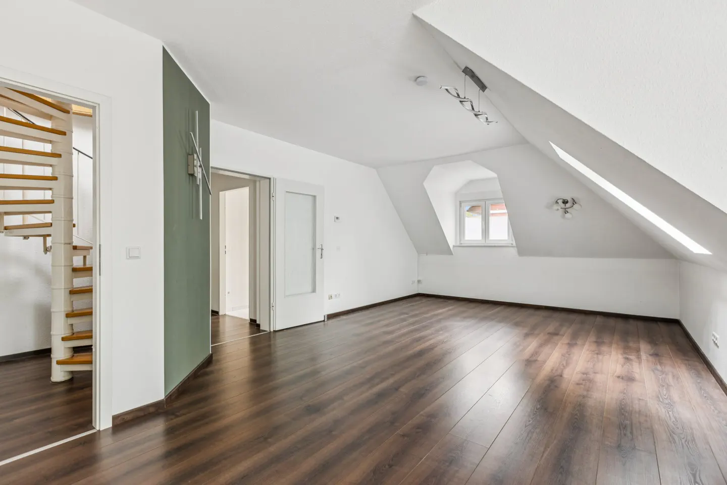 Attic room with dark wood floors, white walls, and a spiral staircase. A window is visible in the sloped ceiling.