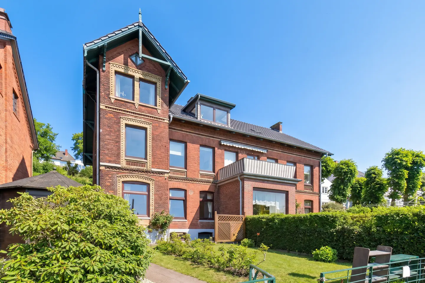 Exterior of a three-story red brick house with green trim and a well-manicured lawn on a sunny day.