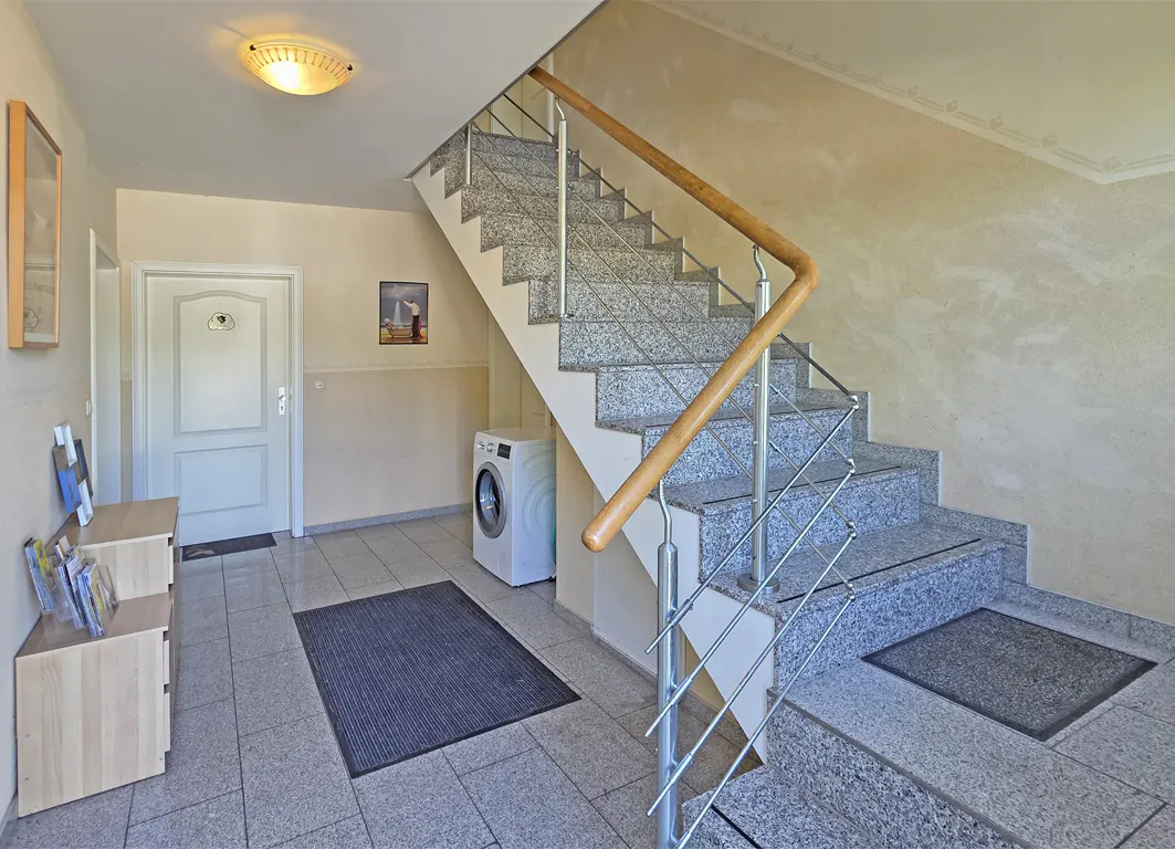 Interior view of a building entrance with a granite staircase, a white door, a washing machine, and a wooden handrail.