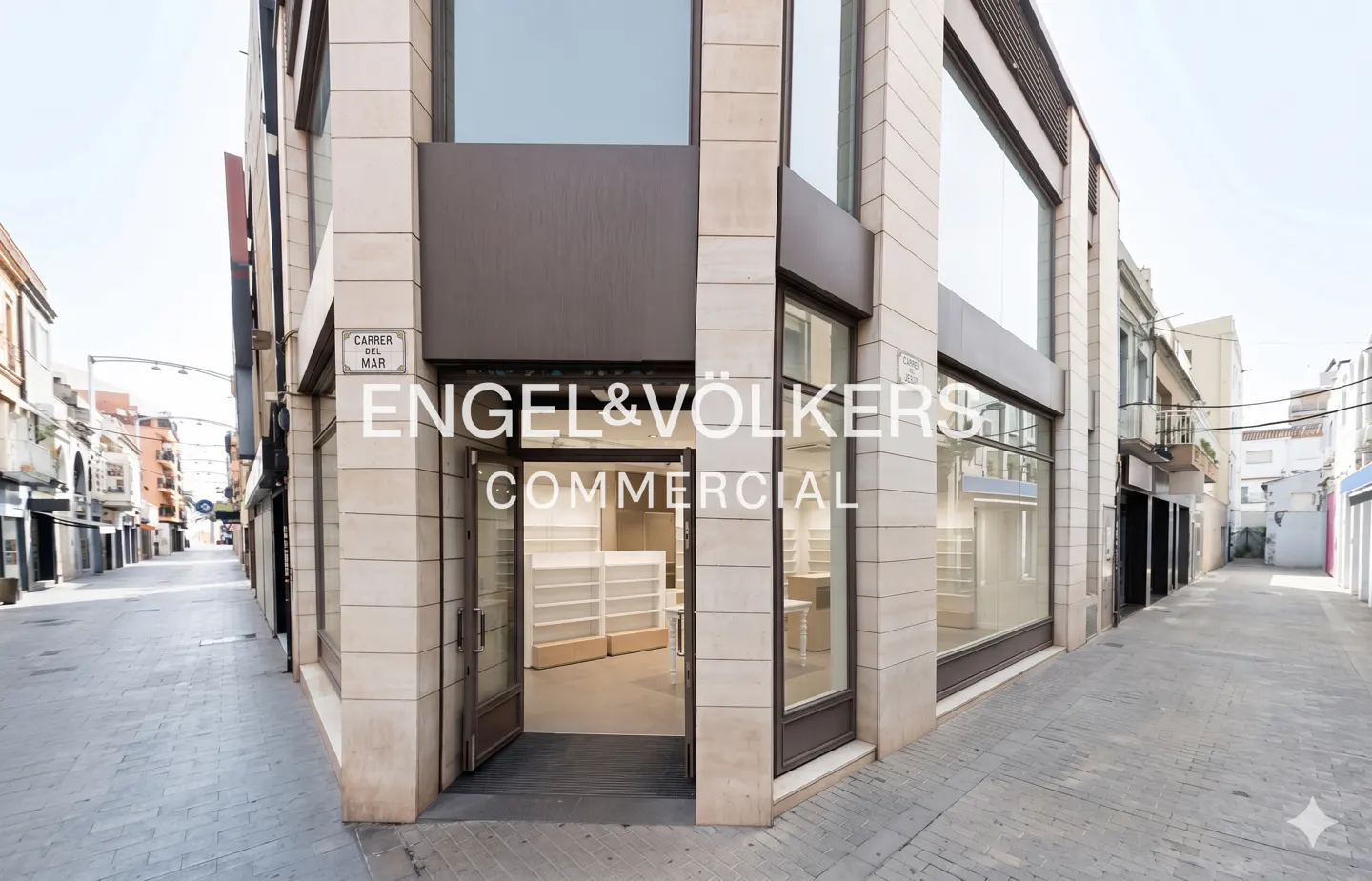 Engel & Völkers Commercial building exterior on a quiet street. The building is stone with large windows and an open door.