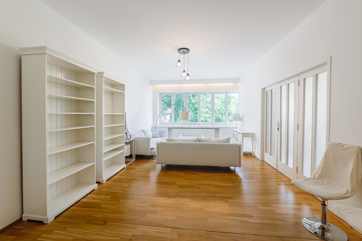 Bright living room with white walls, hardwood floors, two tall bookshelves, a white sofa, and a modern swivel chair.