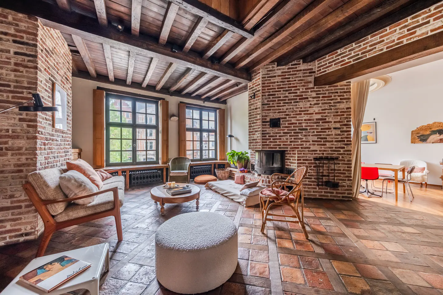Rustic living room with exposed brick walls, wooden beamed ceiling, terracotta tile floor, fireplace, and cozy furniture.