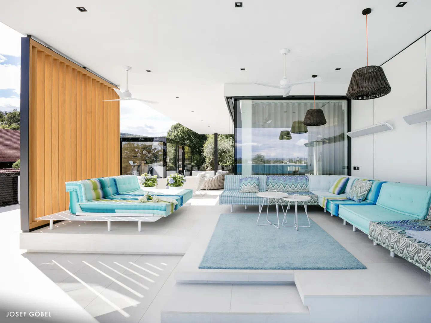 Modern outdoor patio with bright turquoise sectional seating, a light blue rug, and a wooden privacy screen.