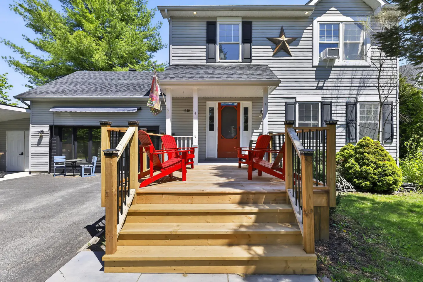 Exterior of a two-story gray house with a wooden porch and red Adirondack chairs.