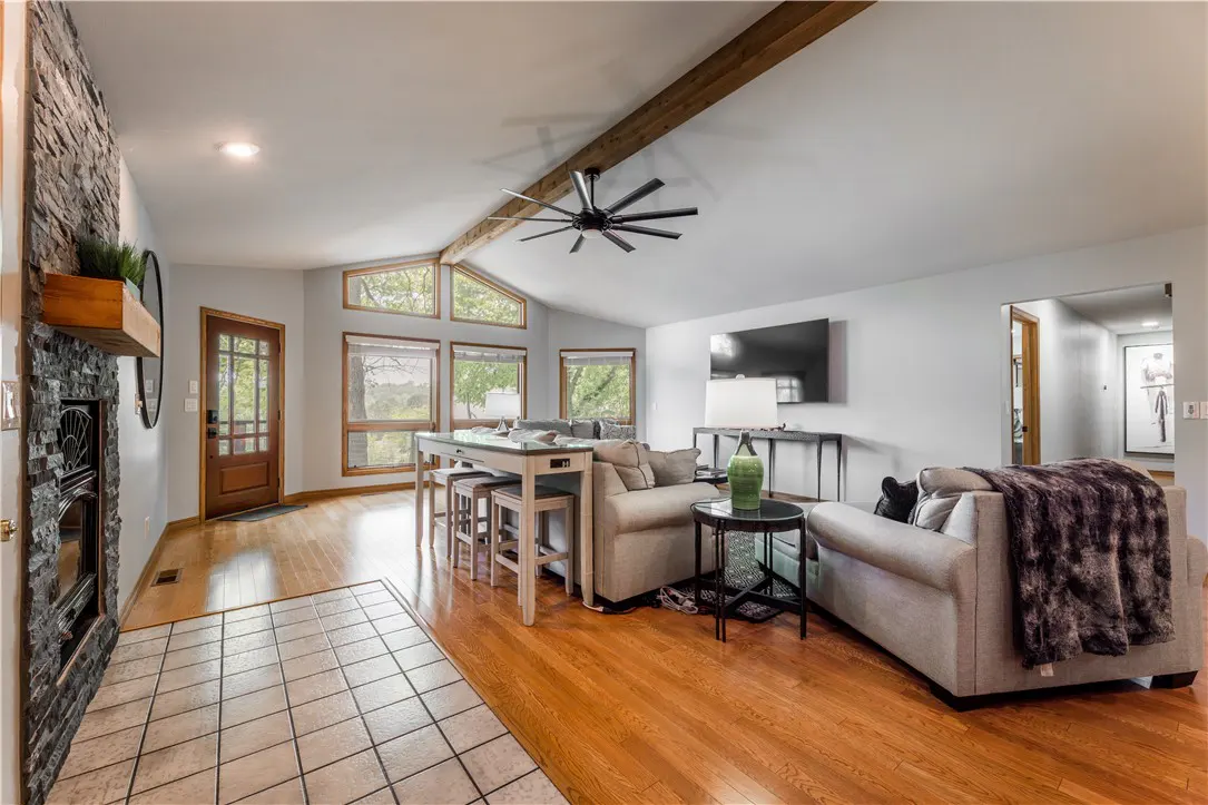 Open-concept living room with hardwood floors, stone fireplace, and large windows. Beige sofas and a high table with stools are visible.