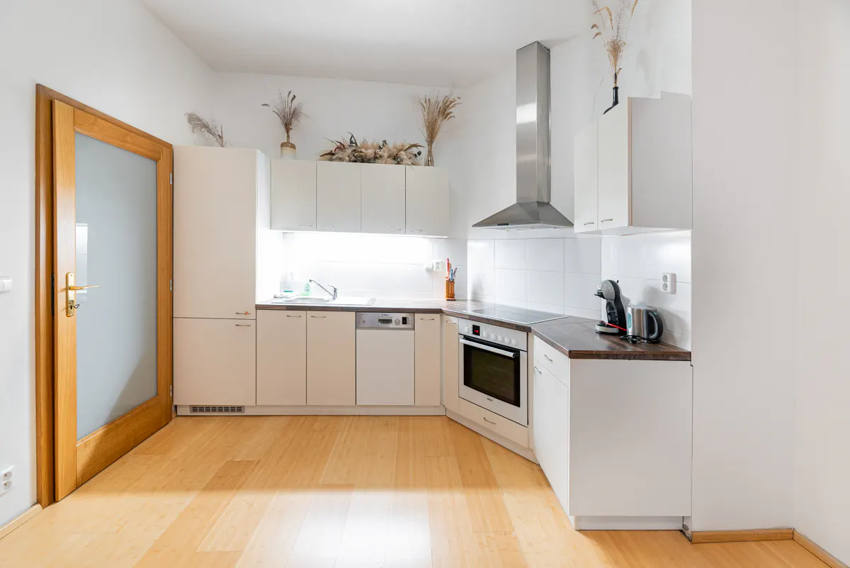 Bright kitchen with white cabinets, stainless steel hood, and wood floor. A wood-framed glass door is on the left.