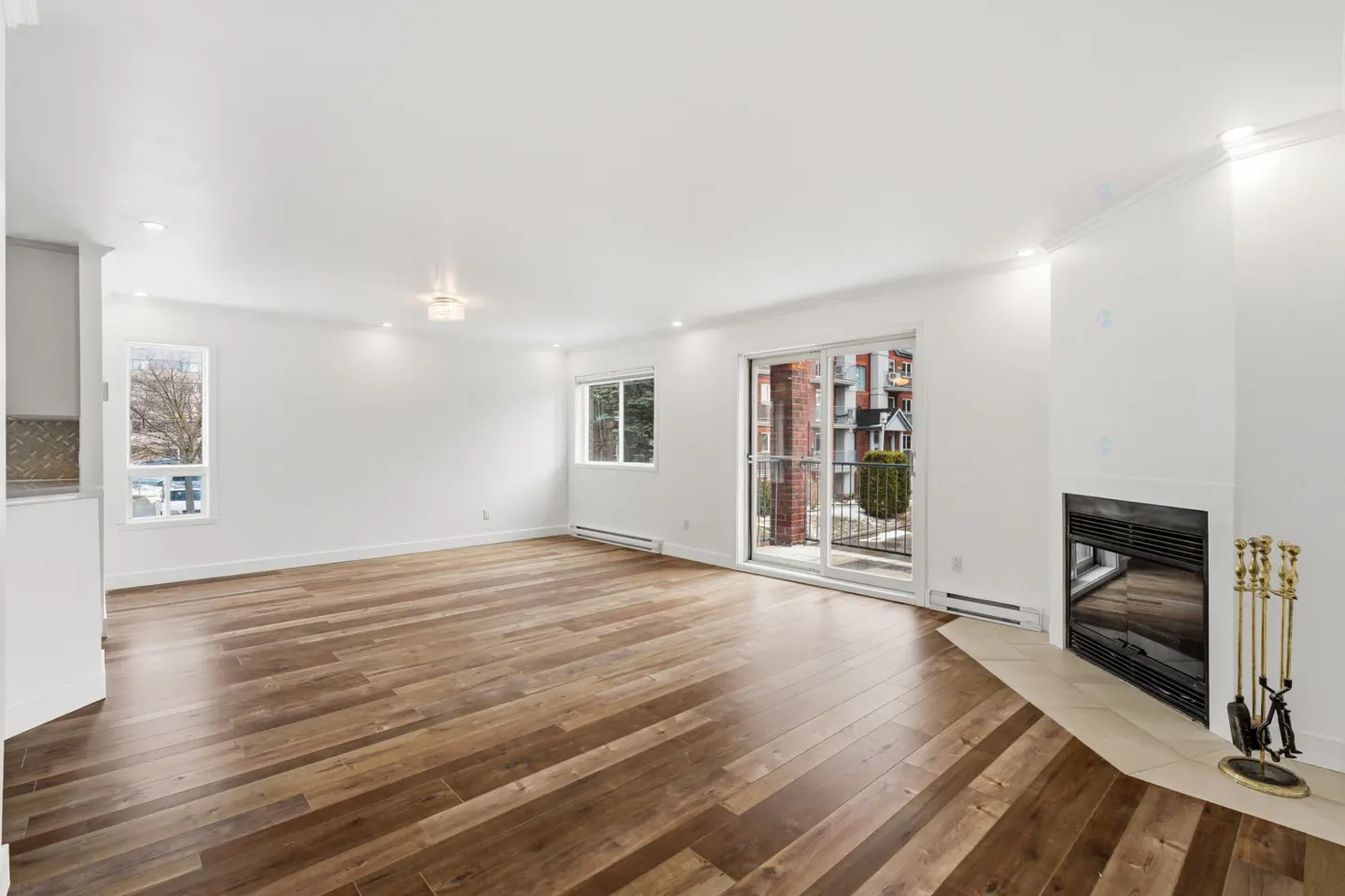 Bright, empty living room with hardwood floors, white walls, fireplace, and sliding glass doors to a balcony.