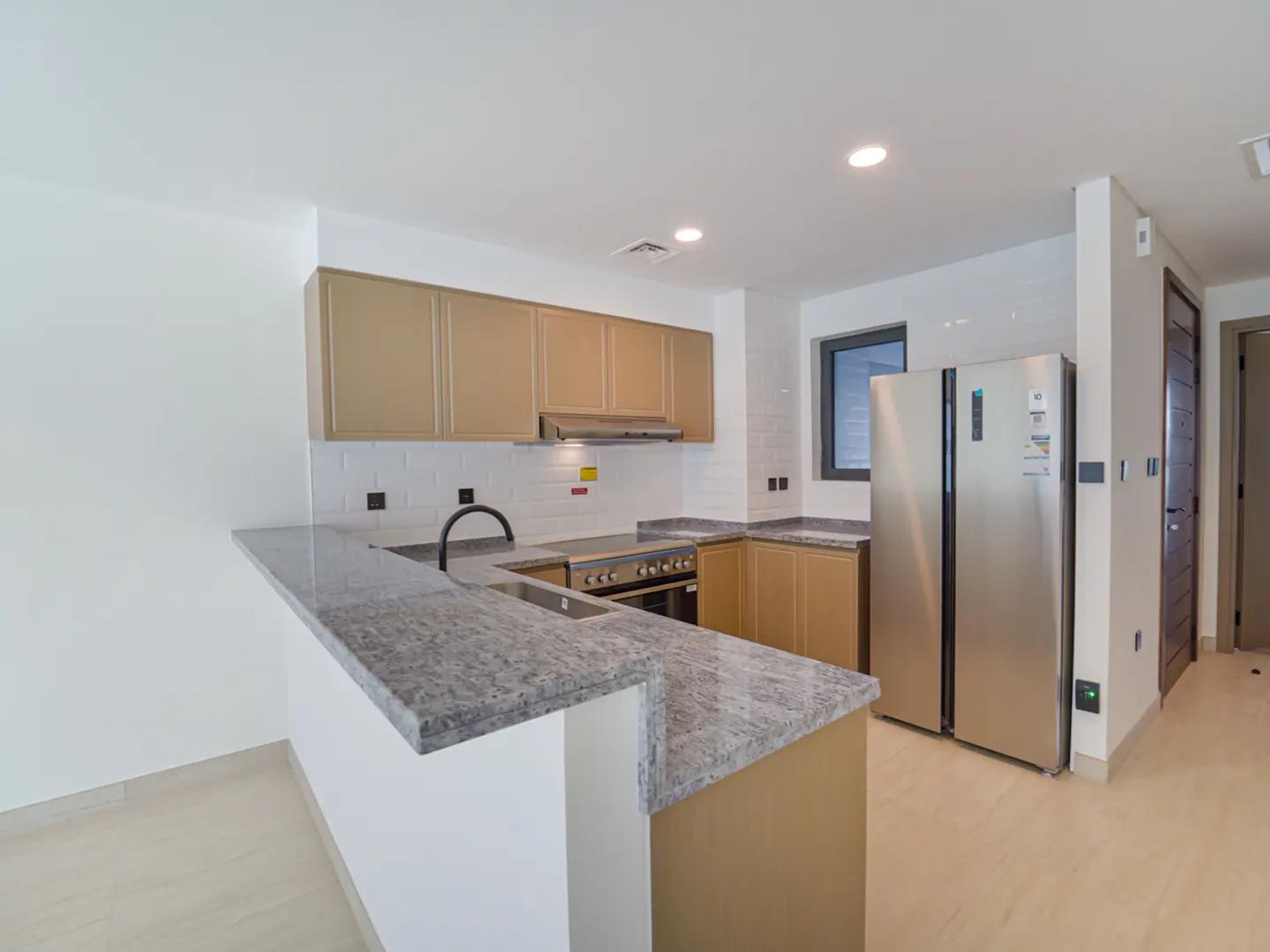 A modern kitchen with tan cabinets, granite countertops, stainless steel appliances, and white subway tile backsplash.