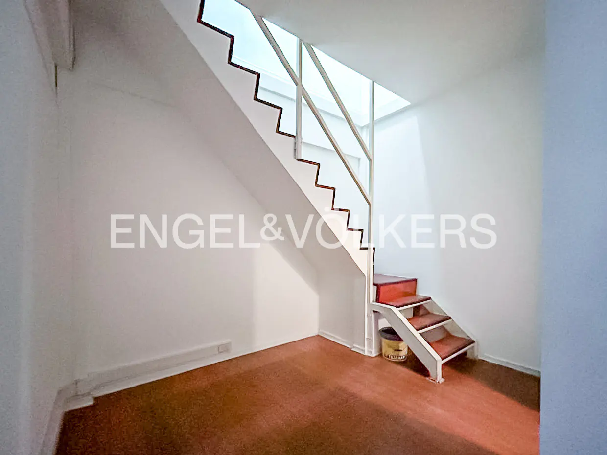 Interior view of a room with a wooden floor, white walls, and a staircase with red steps. The Engel & Volkers logo is visible on the wall.
