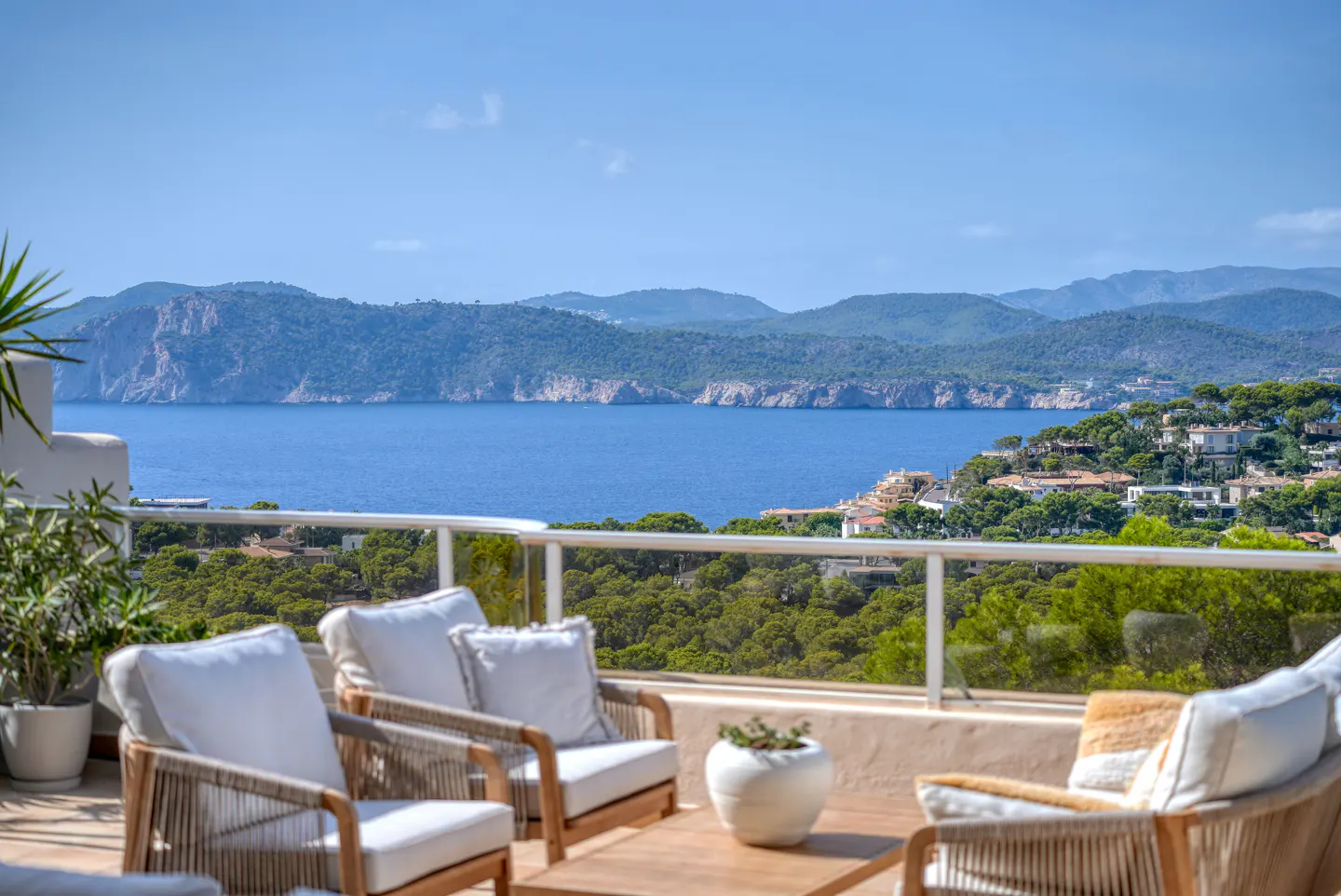 Outdoor patio with four chairs, a table, and a view of the ocean and mountains on a sunny day.