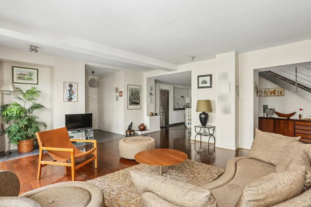 Bright living room with hardwood floors, tan sofa, leather accent chair, round coffee table, and view into the kitchen.