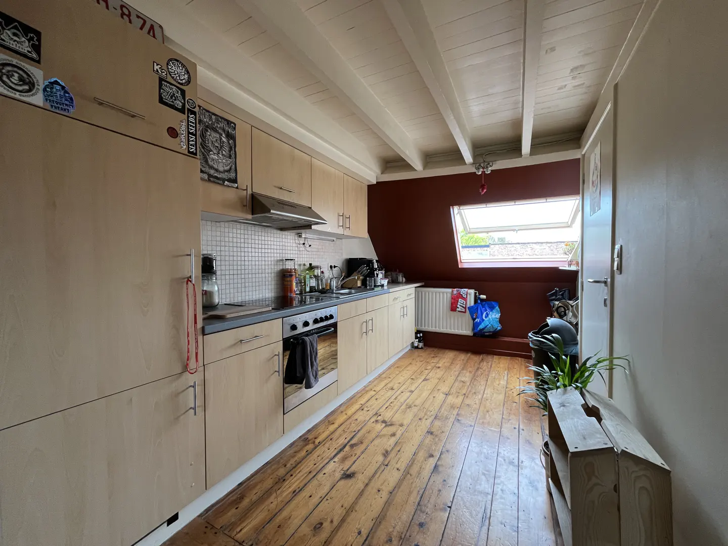 A kitchen with light wood cabinets, a white ceiling with beams, and a red accent wall. A skylight is visible.