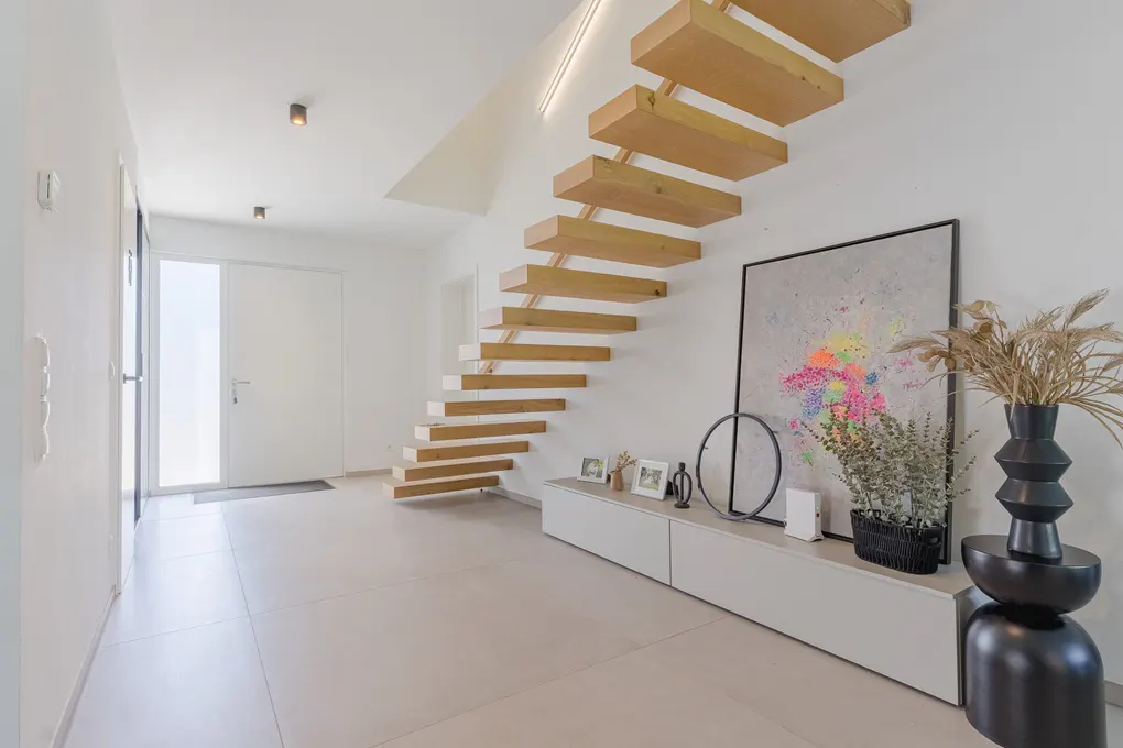 Modern entryway with light wood floating staircase, white walls, tiled floor, and a console table with abstract art.