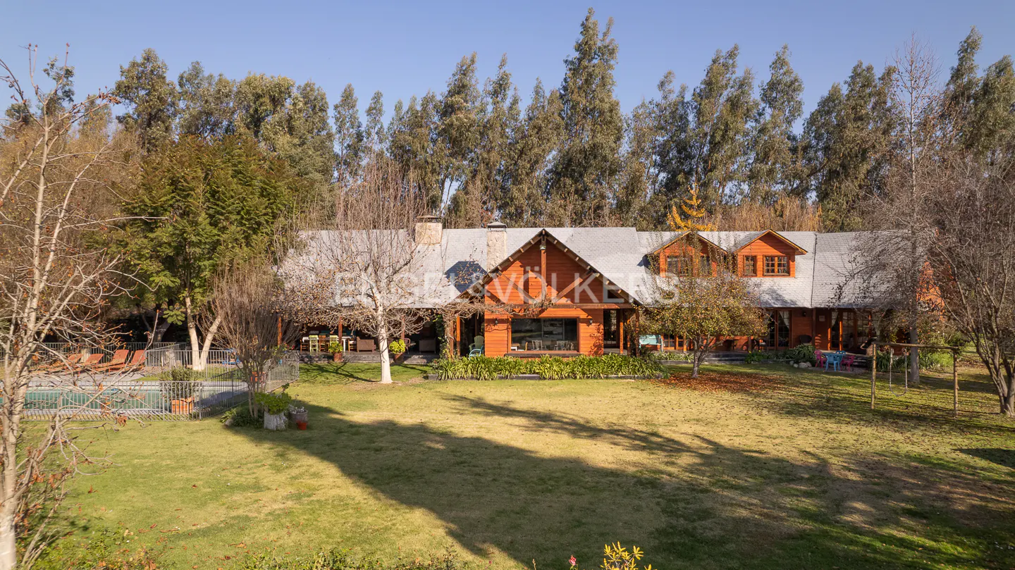Exterior view of a two-story, orange wood house with a gray roof, green lawn, pool, and tall trees.