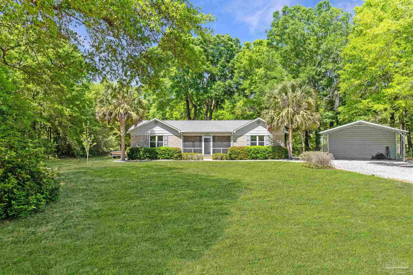 A single-story gray house with a gray roof and a large green lawn, surrounded by trees and a gray carport.
