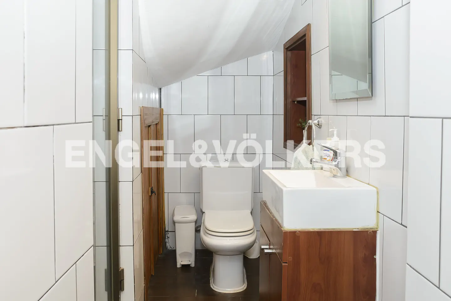 Tiled bathroom with white toilet, sink with wood cabinet, and trash can.