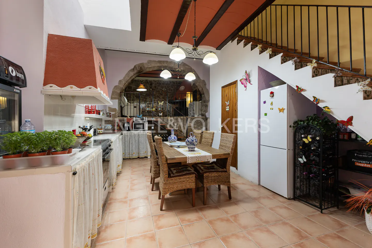 A kitchen and dining area with terracotta tile floors, a wooden table with wicker chairs, and a white refrigerator decorated with butterfly magnets.