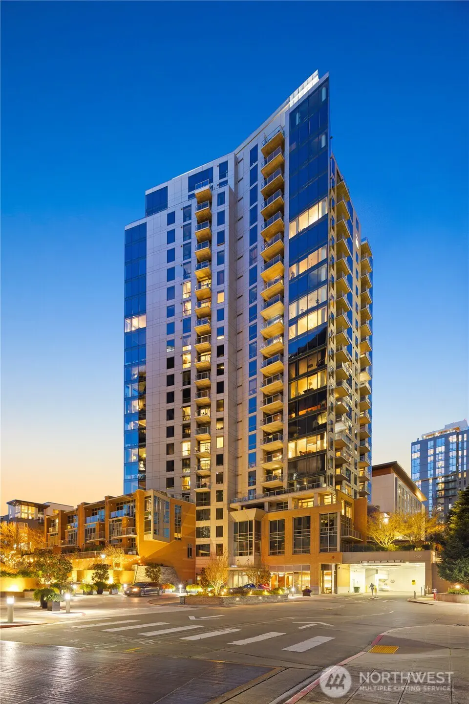 Modern high-rise condo building with blue glass and balconies at dusk.
