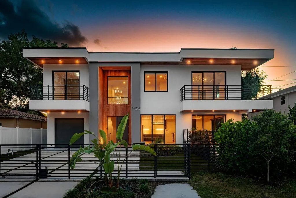 Modern two-story white house with black railings and a wood accent wall at dusk.